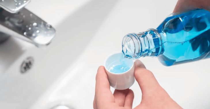 Person rinsing with mouthwash in front of a mirror